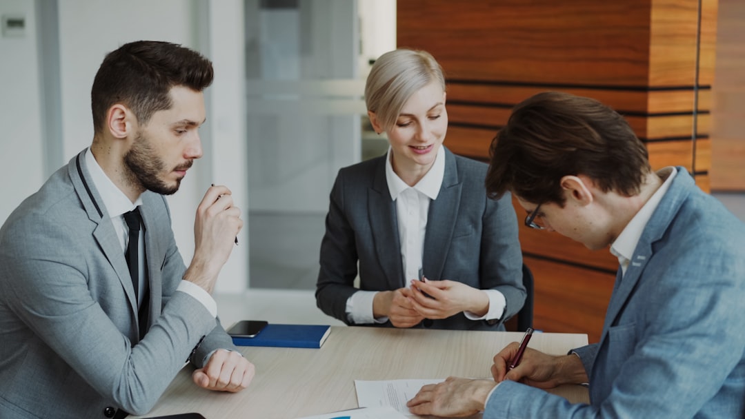 services-01 Young businessman in suit signing contract with his colleague while corporate lawyer explaining details of partnership sitting in modern office indoors