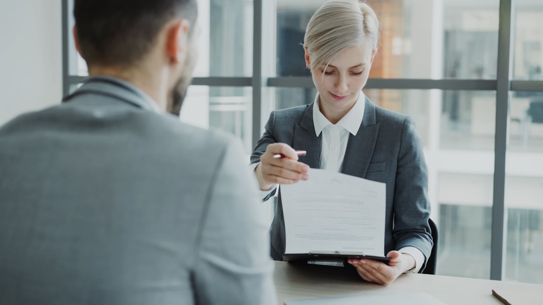 services-03 HR businesswoman having job interview with young man in suit and watching his resume application in modern office indoors